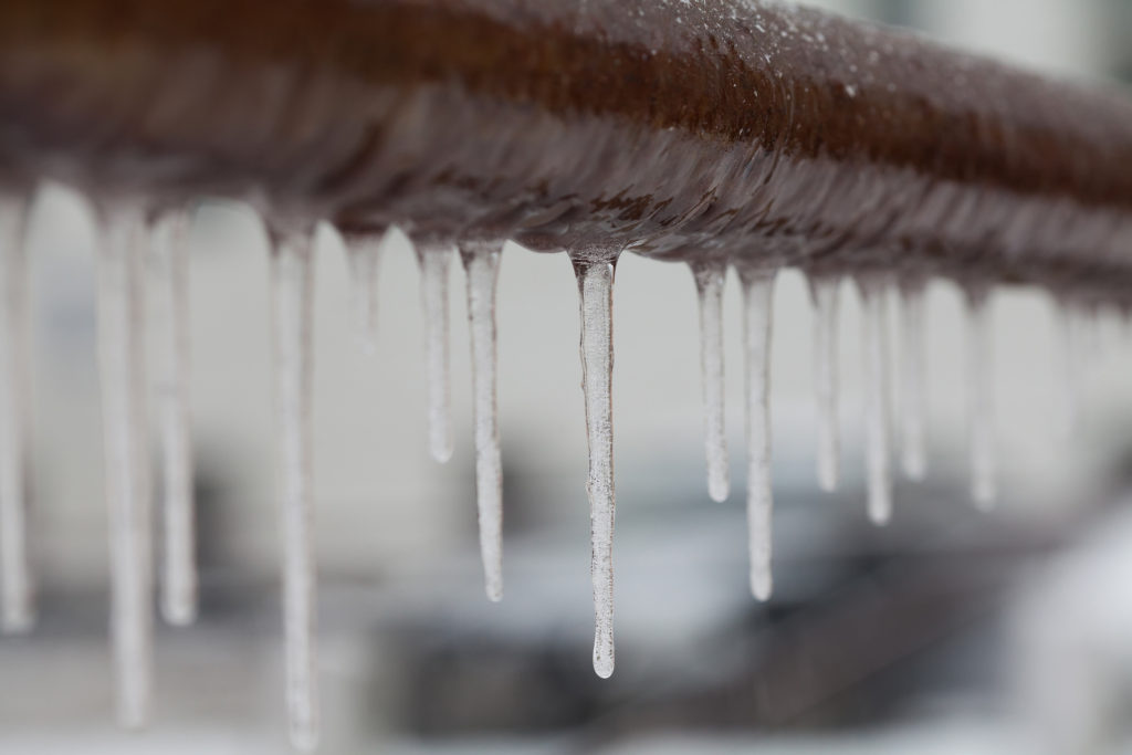 Icicles hanging from a brown pipe. Frozen water and metal surface, winter time concept. 